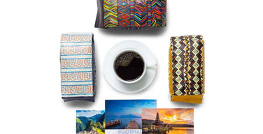 Three Atlas Coffee Club coffee bags in bold patterned packaging around a cup of black coffee, with postcards from Peru, Guatemala, and Indonesia
