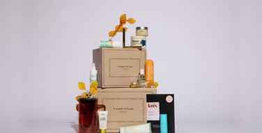 Two stacked kraft FabFitFun Fall 2026 boxes surrounded by the season’s products: a French press, skincare tubes and jars, a candle, and a knix card, on a pale lavender backdrop