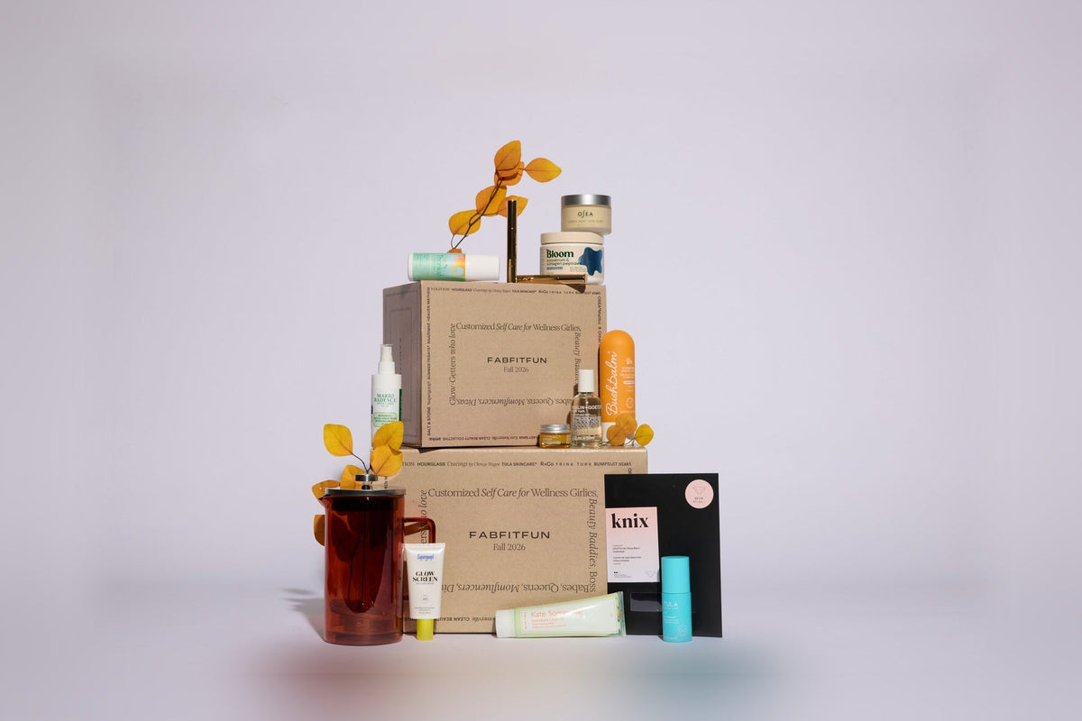 Two stacked kraft FabFitFun Fall 2026 boxes surrounded by the season’s products: a French press, skincare tubes and jars, a candle, and a knix card, on a pale lavender backdrop