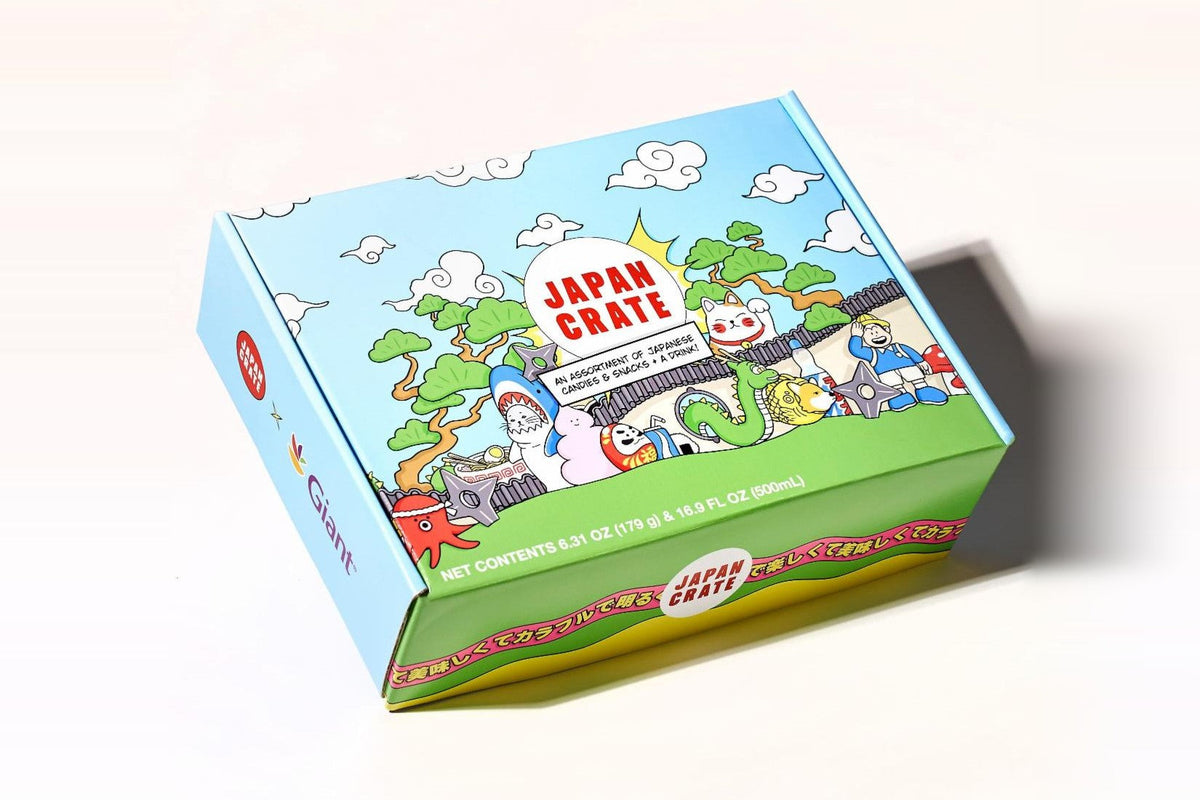 A Japan Crate box printed with the red Japan Crate logo, cartoon clouds, pine trees, a lucky cat, and a dragon, labeled as an assortment of Japanese candies and snacks plus a drink