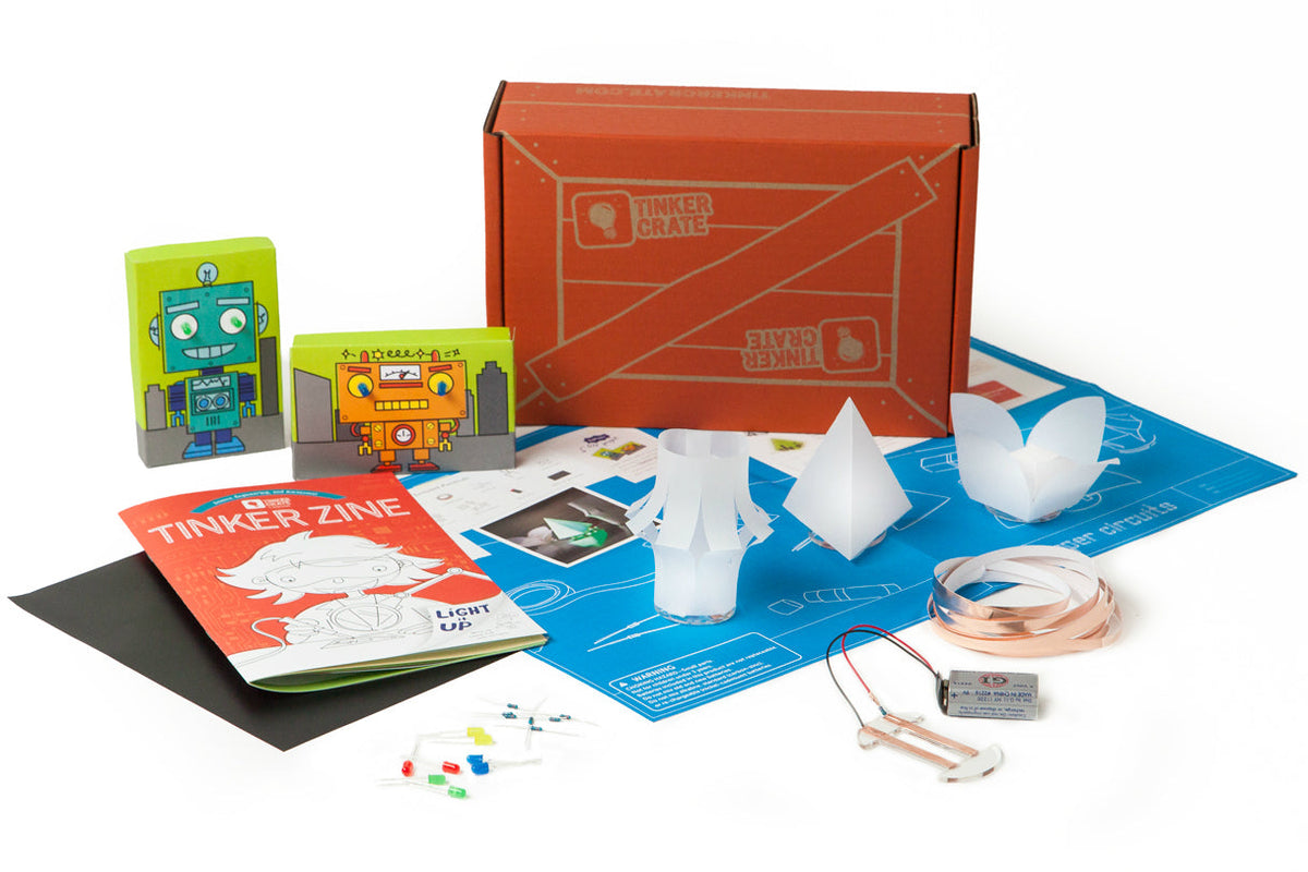 KiwiCo Tinker Crate box with its Tinker Zine booklet and a paper circuits kit: LEDs, copper tape, a 9-volt battery, an instruction sheet, and three folded paper lamp shades.