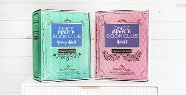 Two Once Upon a Book Club book-shaped boxes on a white dresser, a teal Young Adult box and a pink Adult box, each with the Once Upon a Book Club logo