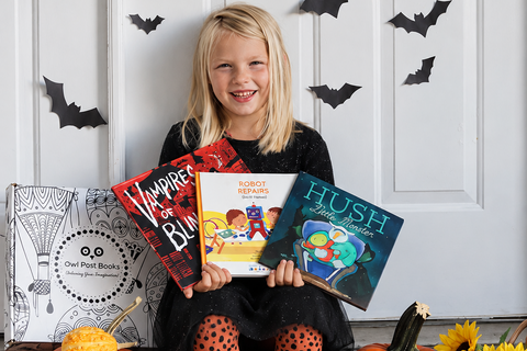 Child holding three books from her Owl Post Books kids book club surrounded by pumpkins and Halloween decorations