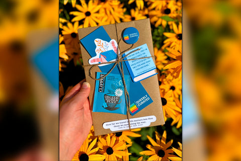 Book wrapped in brown paper and twine with blue and white items on top, held above yellow flowers with a blurred background