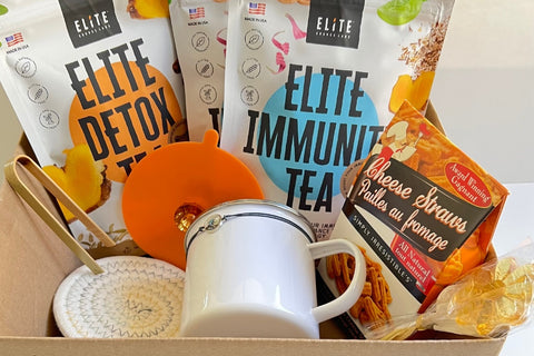 Elite positiviTea box with organic herbals supports immune and digestive systems. Elite tea box has a cup, lid, placemate, snack, honey