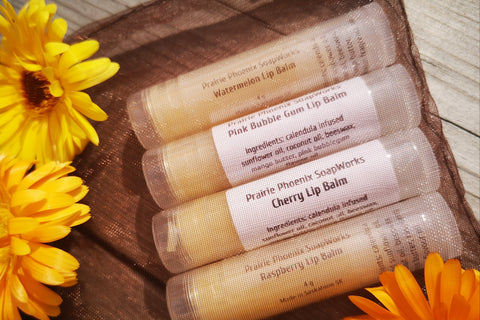 4 Natural, homemade lip balms in an organza bag, surrounded by the calendula flower they are made with.