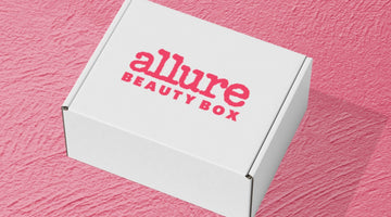 A white Allure Beauty Box shipping box with the pink allure BEAUTY BOX logo, on a pink textured surface