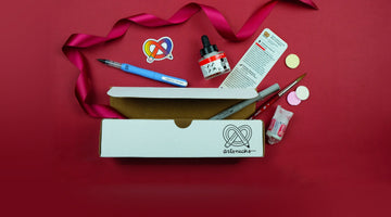 An open white ArtSnacks box printed with the pretzel-and-pencil artsnacks logo, with the August menu card, Amsterdam acrylic ink, a Zig letter pen, a Faber-Castell pen, a Princeton brush, a sticker, and Necco wafers on red paper