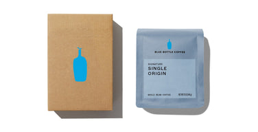 A Blue Bottle Coffee shipping box with the blue bottle logo beside a 12-ounce bag of Signature Single Origin whole bean coffee