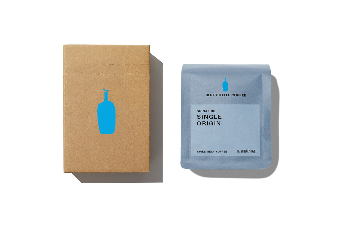 A Blue Bottle Coffee shipping box with the blue bottle logo beside a 12-ounce bag of Signature Single Origin whole bean coffee