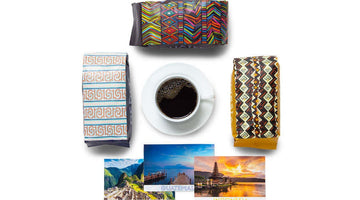 Three Atlas Coffee Club coffee bags in bold patterned packaging around a cup of black coffee, with postcards from Peru, Guatemala, and Indonesia