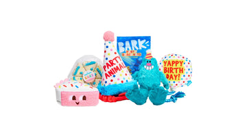 BARK’s Birthday Box assortment: a plush cake slice, a party-hat toy, a bag of BARK treats, a teal monster plush, and a balloon-shaped toy
