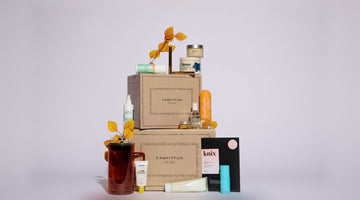 Two stacked kraft FabFitFun Fall 2026 boxes surrounded by the season’s products: a French press, skincare tubes and jars, a candle, and a knix card, on a pale lavender backdrop