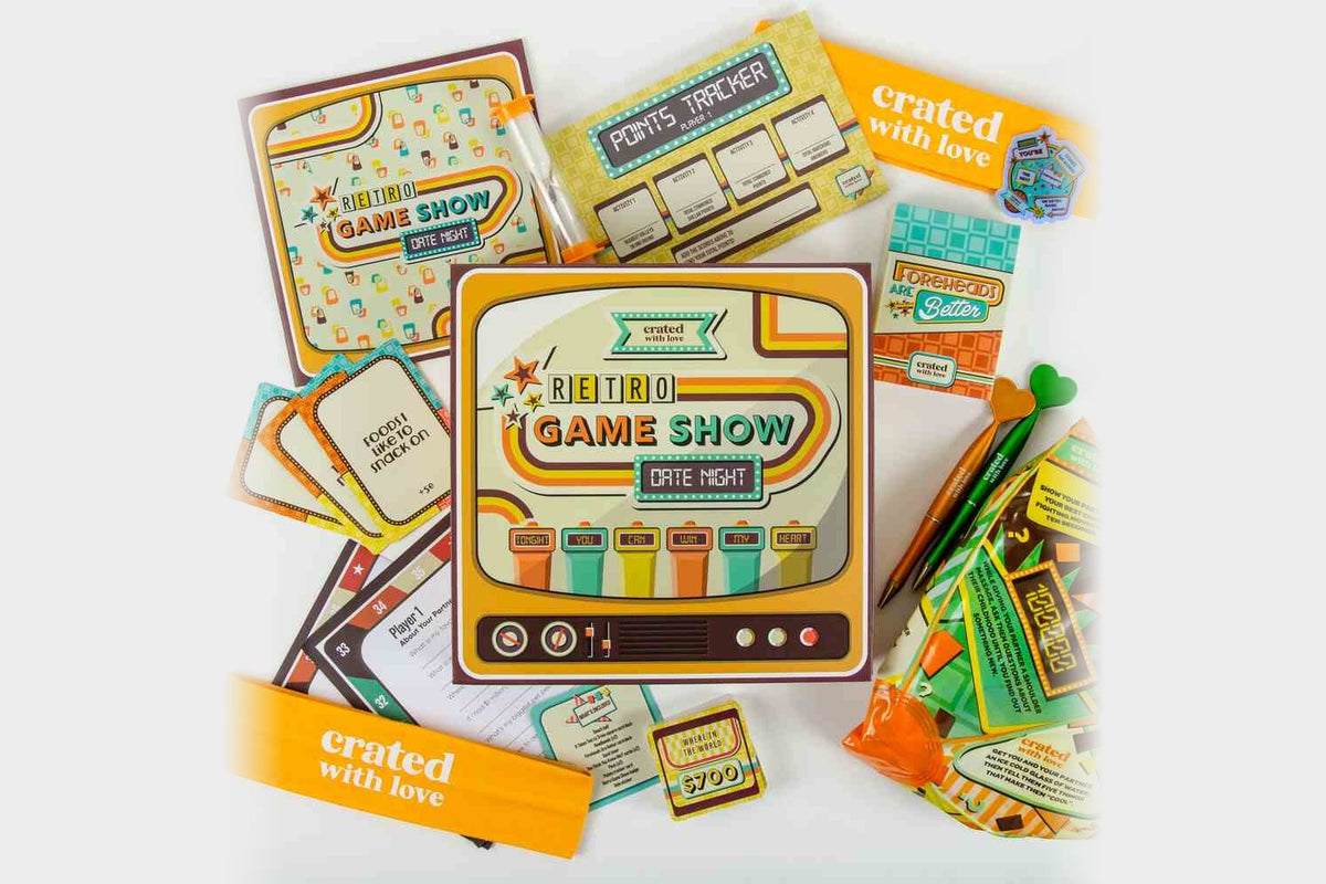 A Crated with Love Retro Game Show date night box surrounded by its game cards, points tracker, pens, and two orange bands printed with the crated with love logo