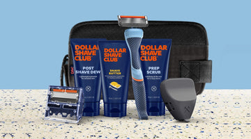 Dollar Shave Club's Fully Loaded Starter Set: Post Shave Dew, Shave Butter, and Prep Scrub tubes with the Dollar Shave Club logo, a blue handle with a six-blade cartridge, a cartridge refill, and a black travel case