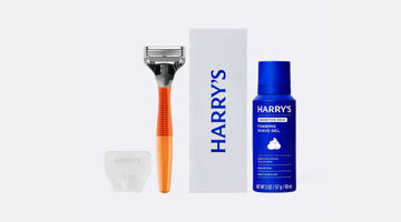 Harry’s Original Starter Set: an orange razor, a white box printed with the Harry’s logo, a blue can of Harry’s foaming shave gel, and a clear travel blade cover