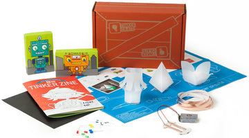 KiwiCo Tinker Crate box with its Tinker Zine booklet and a paper circuits kit: LEDs, copper tape, a 9-volt battery, an instruction sheet, and three folded paper lamp shades.