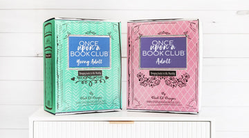 Two Once Upon a Book Club book-shaped boxes on a white dresser, a teal Young Adult box and a pink Adult box, each with the Once Upon a Book Club logo
