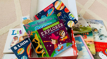 An open red-and-white box printed “Little box, big adventures” on its front edge, holding board books such as This Little Explorer and First Animal Facts: Ocean, with more children’s books spread on a rug around it.