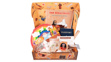 An open Bible Crate box from Good & True Media for Crate 1, From Creation to Abraham, with the Bible Crate activity book, a passport, passport stickers, an intention card, an Abraham character card, and a Noah’s ark rainbow craft