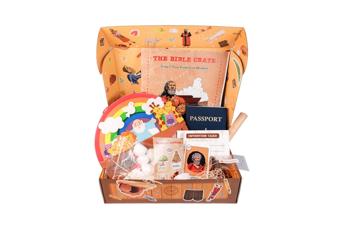 An open Bible Crate box from Good & True Media for Crate 1, From Creation to Abraham, with the Bible Crate activity book, a passport, passport stickers, an intention card, an Abraham character card, and a Noah’s ark rainbow craft