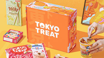 An orange TokyoTreat box printed with the TokyoTreat logo, surrounded by Japanese snacks including Choco Mint Pocky, a Baskin-Robbins Kit Kat, Milky candy, and Cup Noodle Cheese Curry