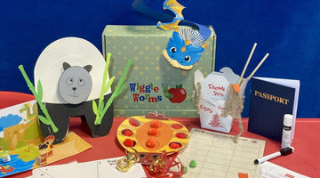A green polka-dot Wiggle Worms Kits box with the Wiggle Worms logo, surrounded by its China kit from the Around the World series: a paper panda, a blue dragon, a takeout box, a toy passport, and a pom-pom game