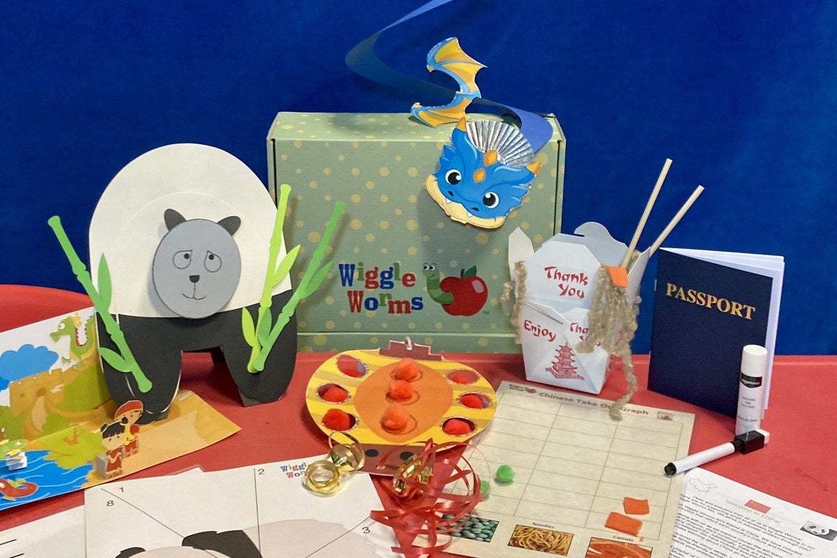 A green polka-dot Wiggle Worms Kits box with the Wiggle Worms logo, surrounded by its China kit from the Around the World series: a paper panda, a blue dragon, a takeout box, a toy passport, and a pom-pom game
