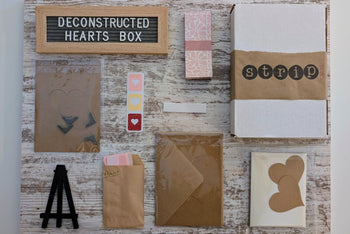 Contents of the Deconstructed Hearts Box including paper bundle, greeting cards, heart cutouts, envelope seals, foam pop dots, and an easel.
