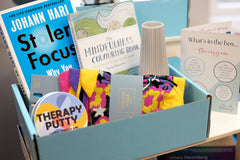 Sample boxes displayed on a crate, showing books, self care items, homeware, information cards, crafts and more