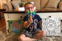 Smiling child with craft and Owl Post Books kids subscription box, a holiday book club gift that brings joy and inspires young readers.