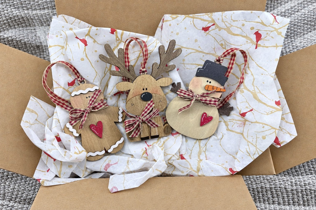 One shipment opened: the wooden gingerbread man, reindeer and snowman ornaments with gingham ribbons on cardinal tissue in a mailer