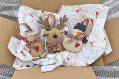 One shipment opened: the wooden gingerbread man, reindeer and snowman ornaments with gingham ribbons on cardinal tissue in a mailer