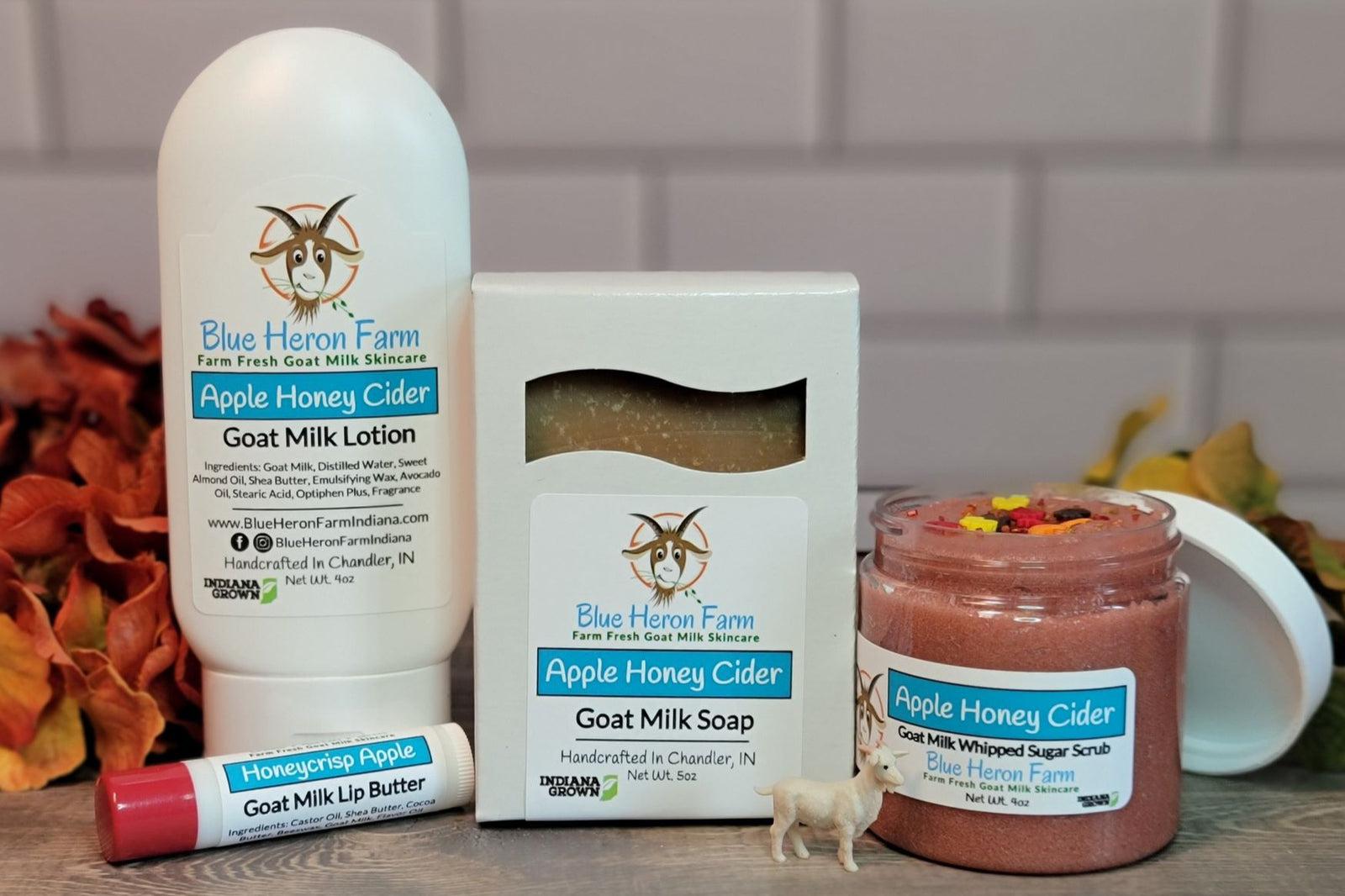 Goat milk lotion, soap, sugar scrub, and lip butter in Honey Apple Cider scent surrounded by fall foliage.