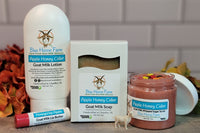 Goat milk lotion, soap, sugar scrub, and lip butter in Honey Apple Cider scent surrounded by fall foliage.