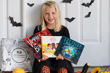 Child holding three books from her Owl Post Books kids book club surrounded by pumpkins and Halloween decorations