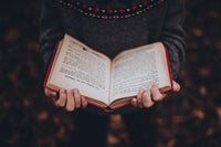 A person holding an open hardcover book with red edges, showcasing a cozy reading moment for book lovers with the Fantasy Books Club subscription