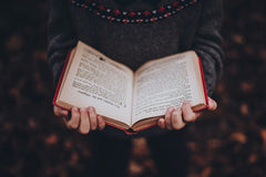 A person holding an open hardcover book with red edges, showcasing a cozy reading moment for book lovers with the Fantasy Books Club subscription