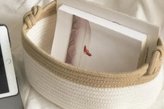 White and brown rope storage basket holding a book with a shoe, on a comfoter and with a tablet in the background