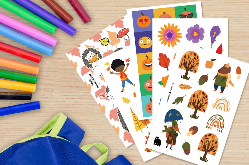 A selection of autumn themed stickers (pumpkins, flowers, trees) pictured on a desktop along with markers and a backpack.