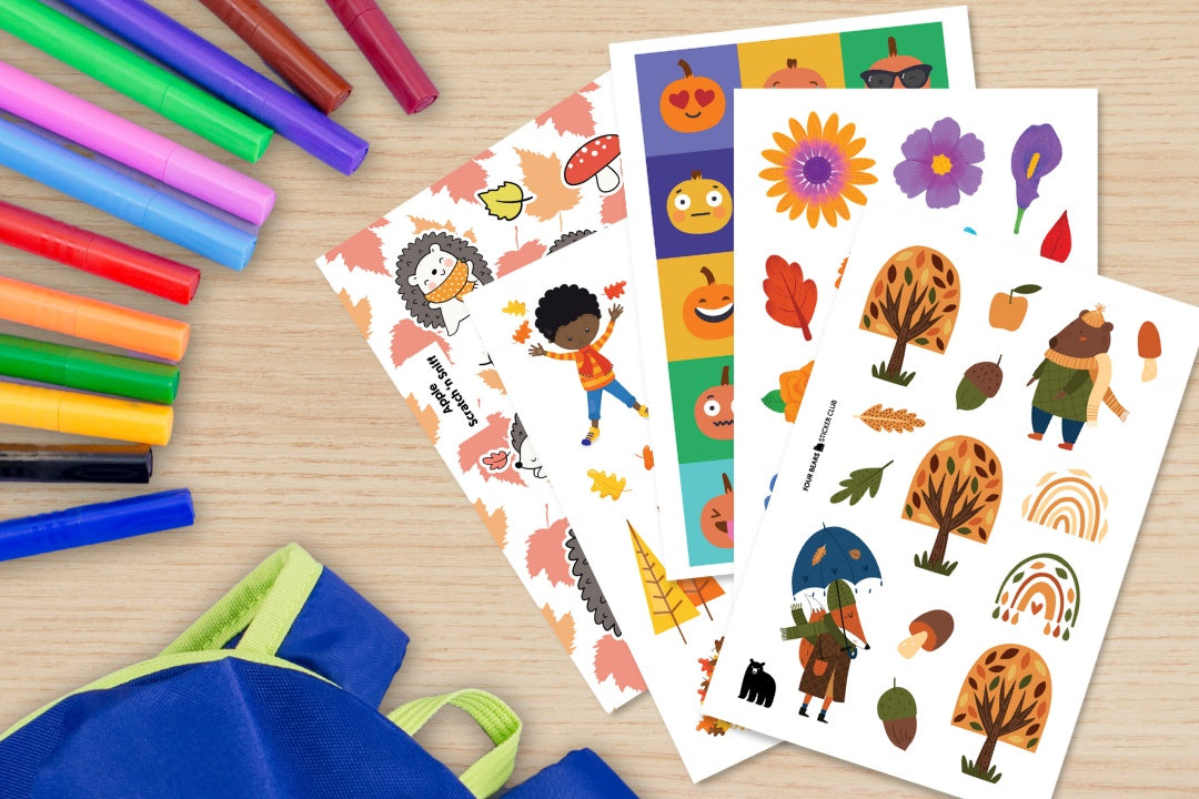 A selection of autumn themed stickers (pumpkins, flowers, trees) pictured on a desktop along with markers and a backpack.