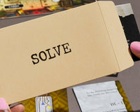 Close up photo of an envelope of a mystery puzzle escape game that has one word on it and it is the word solve.