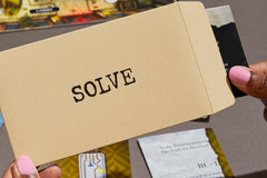 Close up photo of an envelope of a mystery puzzle escape game that has one word on it and it is the word solve.
