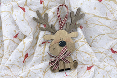 The layered wood reindeer ornament up close: antlers, a glossy black nose, freckled pink cheeks and a red gingham bow on tissue