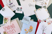 Holiday-themed stationery flat lay with penguins, mistletoe, and “Warm Wishes” cards from My Paper Box in winter pastel colors.