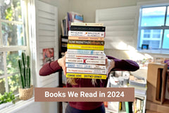 Twelve books stacked in a reader’s hands with the caption 'Books We Read in 2024' in a cozy, sunlit book nook.