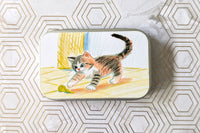 Outside label of one of the catnip tin variants. Featuring a hand drawn kitten, drawn originally using crayon, playing.