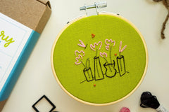 Embroidery project featuring simple pink, gold, and green flower buds with a butterfly. Surrounded by embroidery kit supplies.