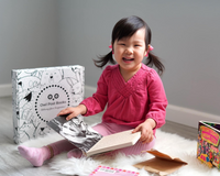 Young child reading beside an Owl Post Books kids subscription box filled with Baby Animals and crafts, a perfect holiday gift for toddlers.
