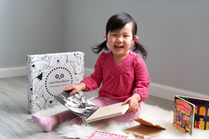 Young child reading beside an Owl Post Books kids subscription box filled with Baby Animals and crafts, a perfect holiday gift for toddlers.